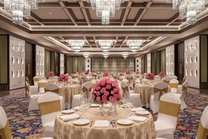 Un salón de banquetes con mesas redondas, sillas blancas y candelabros.