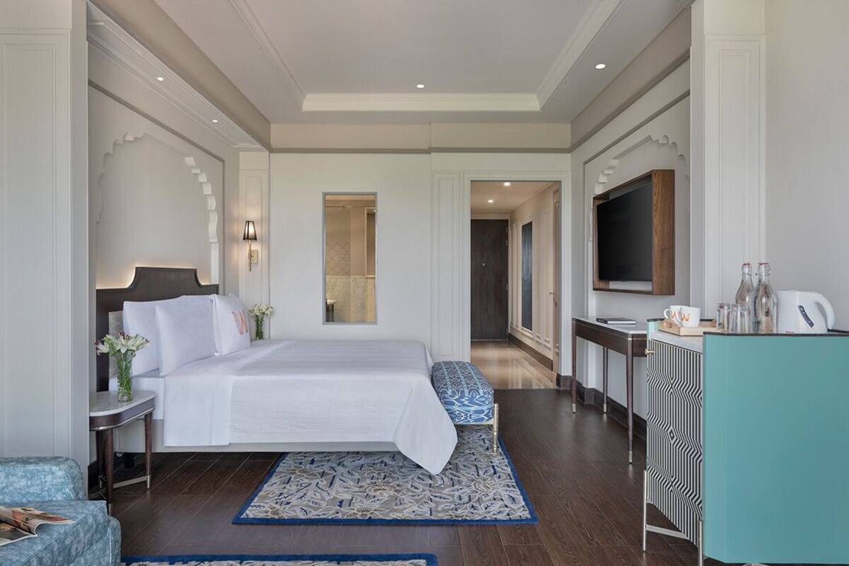 Ruime hotelkamer met een groot bed, een televisie, een bureau met een computer en een badkamer zichtbaar door een geopende deur.