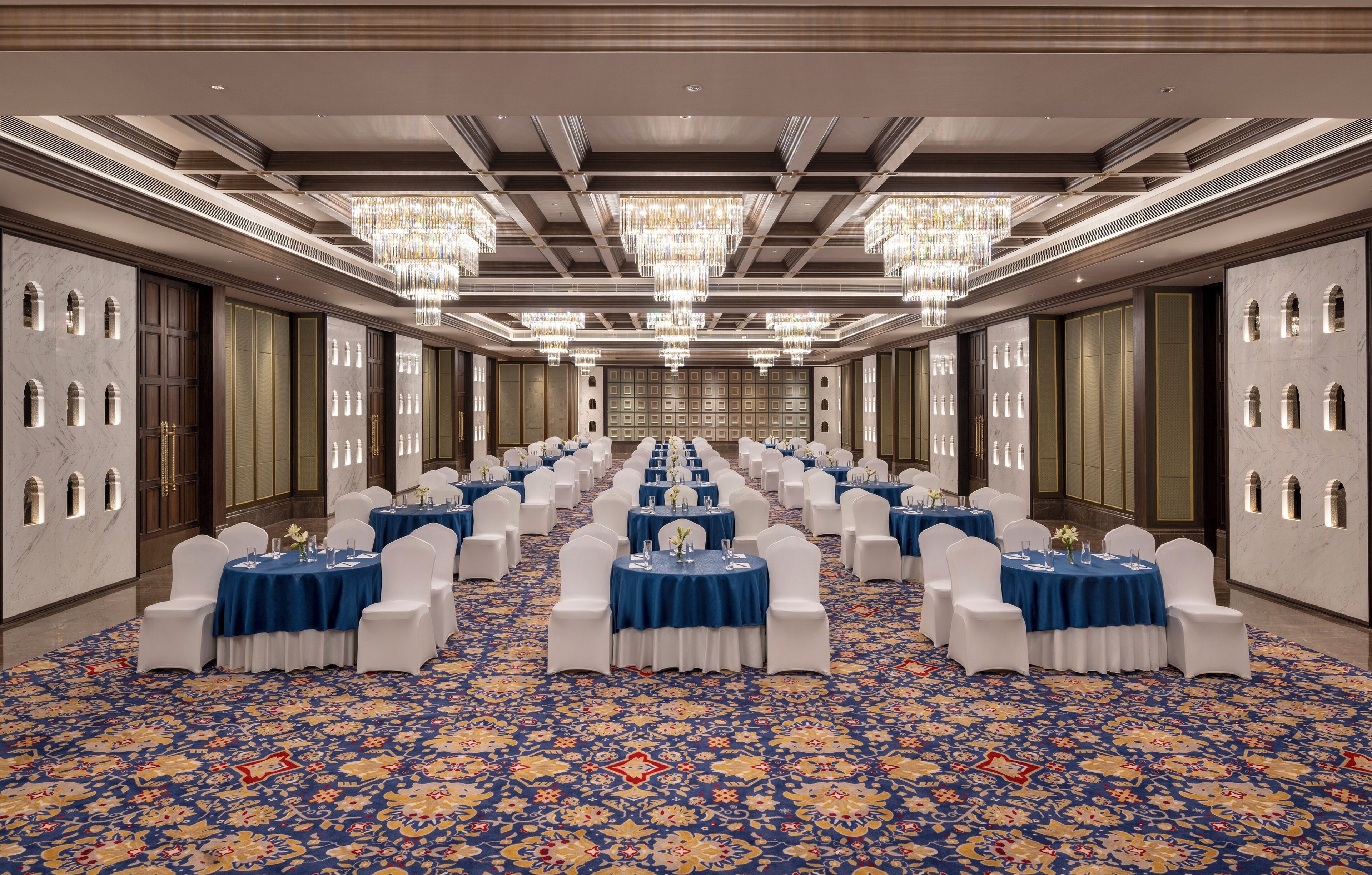 A banquet hall with rows of round tables, white chairs, and blue tablecloths.