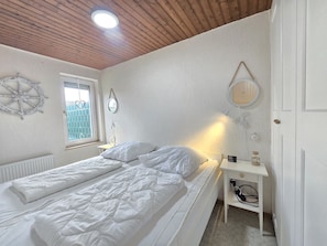 A bedroom with a bed, a bedside table, a mirror, and a window.