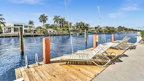 A wooden dock with lounge chairs extending over a pool, surrounded by palm trees and a clear blue sky. - Bay Harbor Sunset Two Bedroom (Bay Harbor Islands)