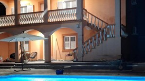 Ein Poolbereich mit einer Treppe zu einem Balkon, umgeben von einem Gebäude mit Bögen und einem Geländer.