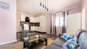 Ein modernes Wohnzimmer mit einem Glastisch, einem grauen Sofa und Blick auf eine Küche und einen Essbereich.