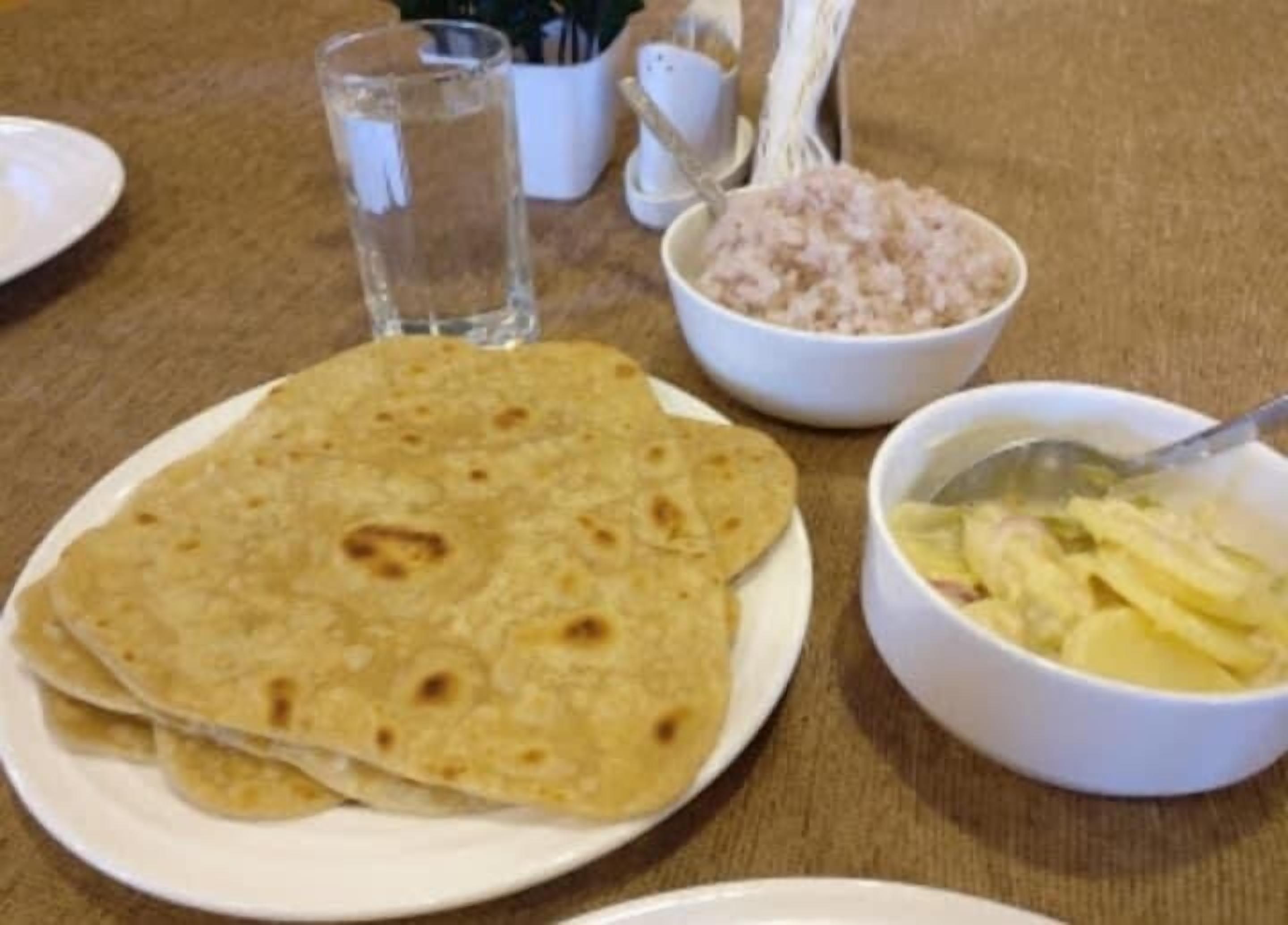 A table with a plate of flatbreads, a bowl of rice, and a bowl of sliced fruit.