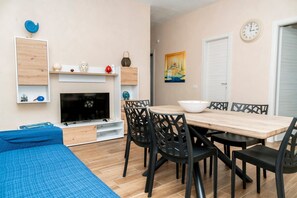 A compact living space with a TV, dining table, chairs, and a bed. - Villino Lella | holiday house in Torre Lapillo (Porto Cesareo)