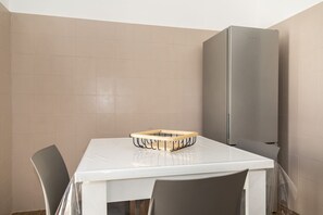 Ein kleiner, sauberer Raum mit einem weißen Tisch, einem grauen Stuhl, einem grauen Kühlschrank und einer Holztablett auf dem Tisch.