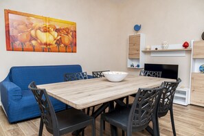A dining area with a wooden table, black chairs, a blue sofa, and a painting on the wall.