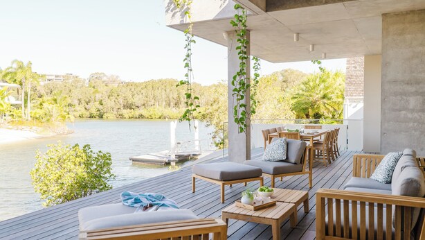 Terraza de madera con mobiliario exterior con vista a un lago, que incluye una estructura de concreto con plantas colgantes.