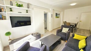A modern living room with a flat-screen TV, grey sofas, a coffee table, and a dining area with a table and chairs. - Blue Sky Ocean Retreat (Larnaca)