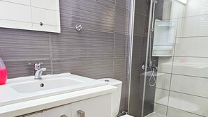 A modern bathroom with a white sink, a toilet, and a glass shower enclosure. - Blue Sky Ocean Retreat (Larnaca)