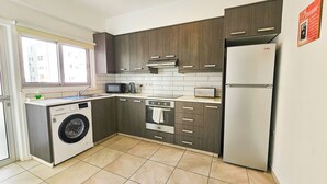 A compact kitchen with a washing machine, microwave, oven, and refrigerator. - Blue Sky Ocean Retreat (Larnaca)