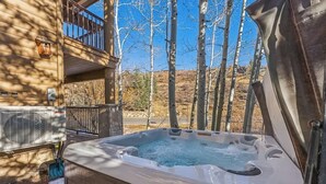 A hot tub with a wooden deck, a balcony, and a view of trees and hills.