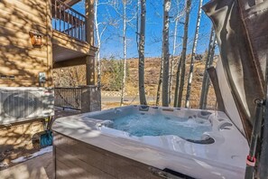 Un bain à remous avec une terrasse en bois, un balcon et une vue sur les arbres et les collines.