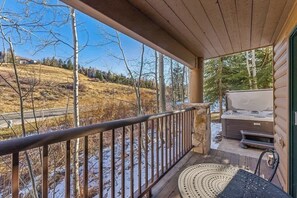 Une véranda couverte offrant une vue sur un paysage enneigé, un barbecue et un jacuzzi.