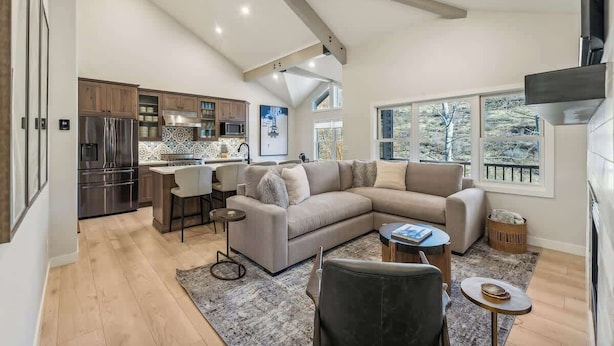 A modern kitchen with built-in appliances, a dining area with a bar, and a living room with a sectional sofa and a fireplace.