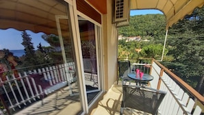 En balkon med et bord og stole, en glasdør og udsigt til en bakke med bygninger.