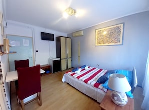Ein Schlafzimmer mit Bett, Schreibtisch, Stuhl, Kleiderschrank, Fernseher und einem Wandbild.