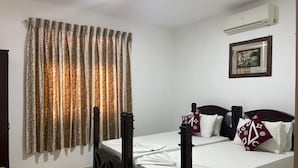 A neatly made twin bed with a headboard, a wall-mounted air conditioner, and a framed picture above it. - Suzuki's Lagoon Front (Katunayaka)