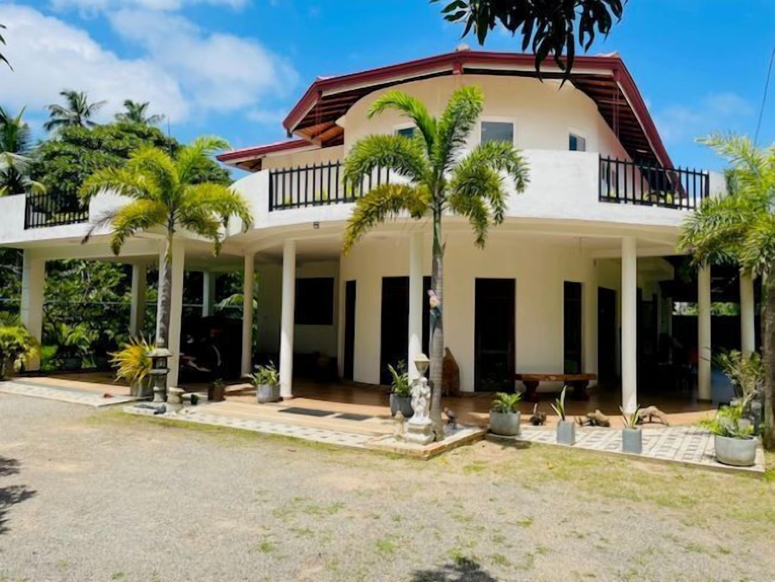 A two-story building with a red roof, white walls, and a covered porch with palm trees.