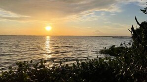 A sunset over a calm body of water with a distant shoreline and a bridge. - Suzuki's Lagoon Front (Katunayaka)