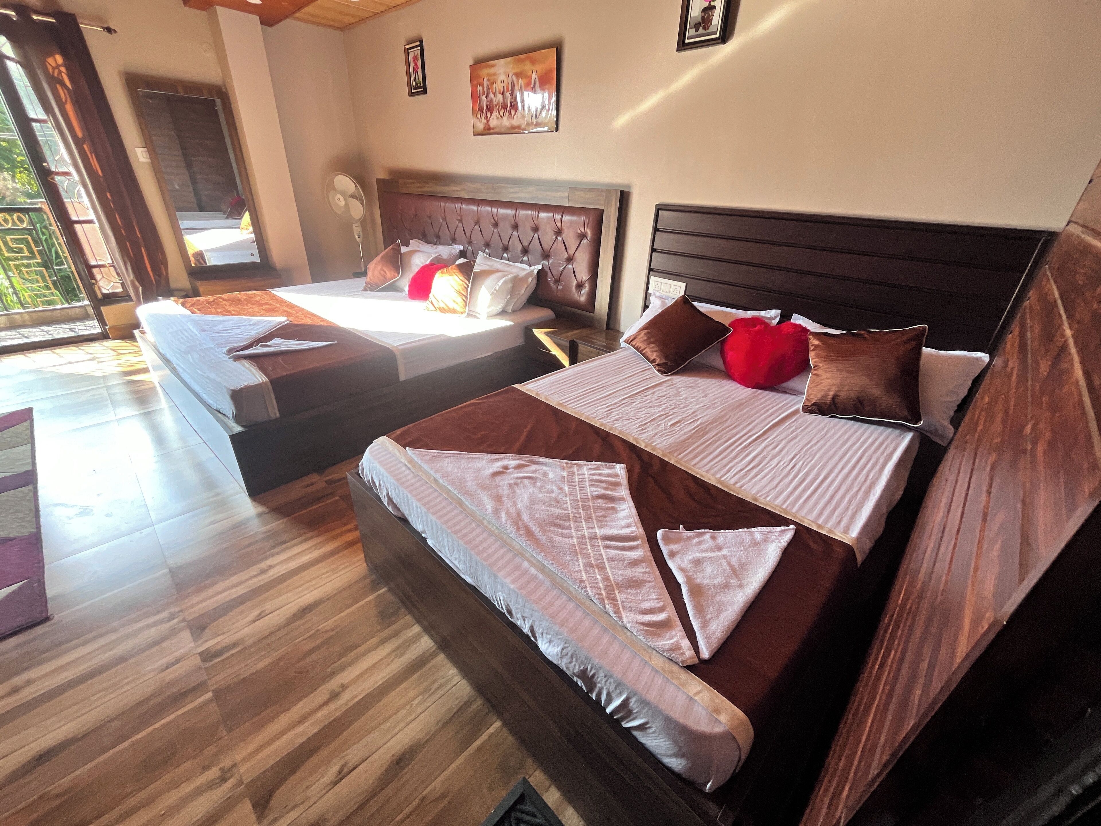 Habitación de hotel con dos camas, suelo de madera, un ventanal grande y un ventilador.