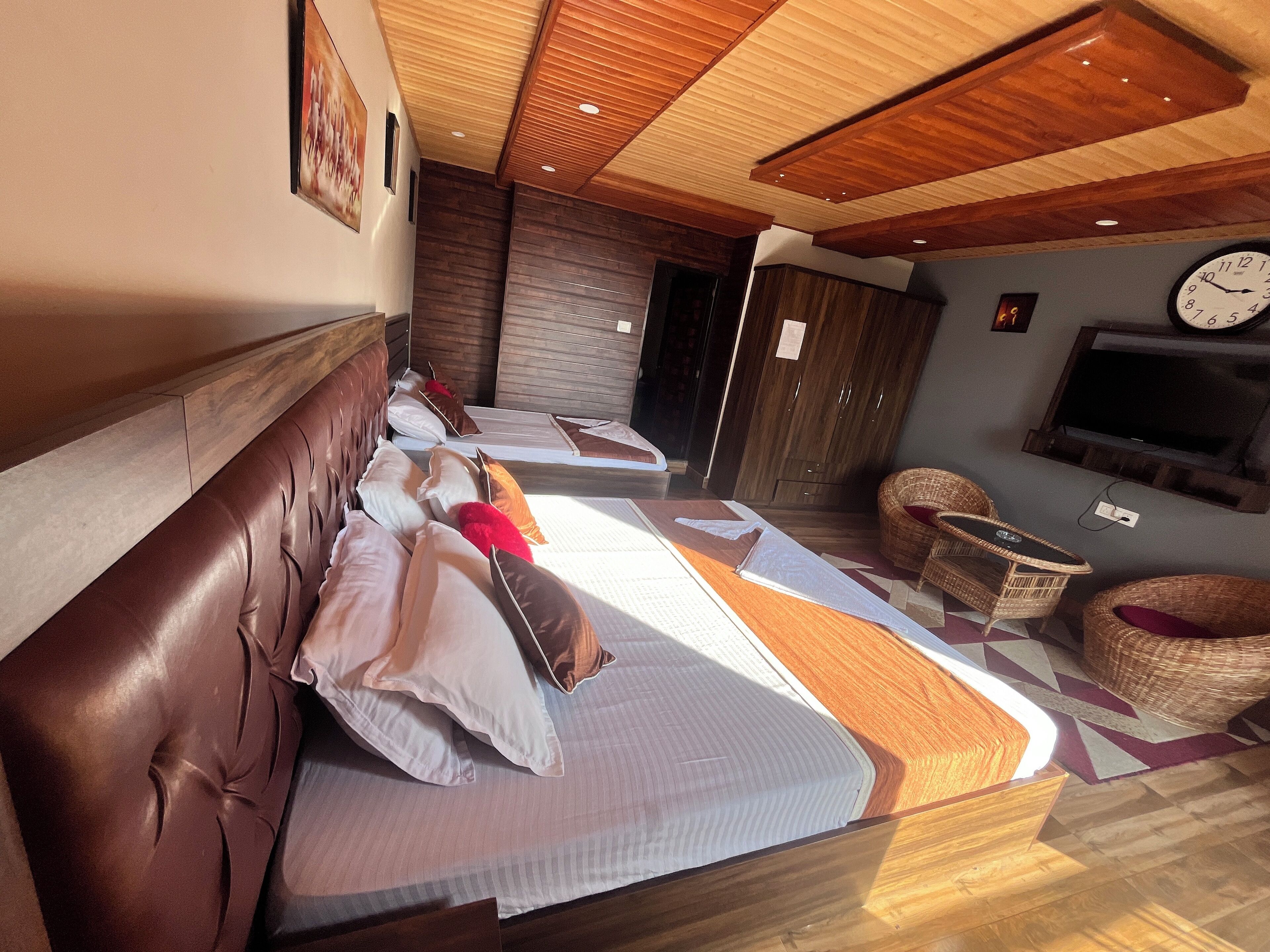 A hotel room with two beds, a TV, a clock, and a seating area with a TV.