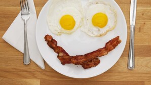 A plate with two fried eggs and a strip of bacon arranged to resemble a smiley face. - TRADITIONAL HOTEL AND RESTAURANT (Kurseong)
