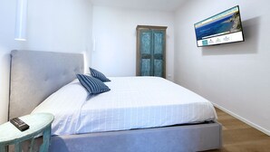 A bedroom with a bed, a small table, a TV on the wall, and a door. - La Perla del Cavo, just a stone's throw from the splendid seafront! (Cavo)