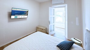 A bedroom with a bed, a small wooden chest, a television mounted on the wall, and a door leading to an outdoor area. - La Perla del Cavo, just a stone's throw from the splendid seafront! (Cavo)