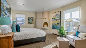 A bedroom with a large bed, a bedside table, a chair, a small table, a fireplace, and large windows. - Casa Feliz I Elegant 2-Bedroom Santa Fe Retreat (Santa Fe)