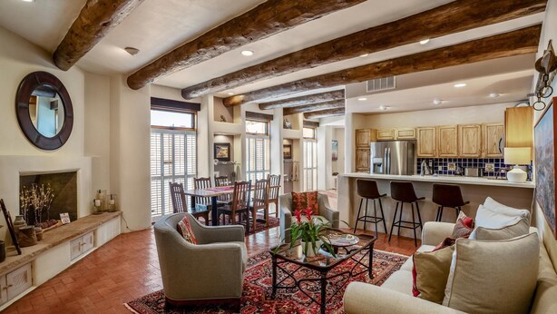 A spacious living area with a fireplace, a dining table with chairs, a kitchen with wooden cabinets, and a large mirror on the wall. - Casa Feliz I Elegant 2-Bedroom Santa Fe Retreat (Santa Fe)