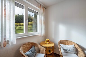 A room with a large window, wicker chairs, a small table with fruit, and a pillow with 'Auszeit' on it.