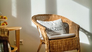 A wicker chair with a cushion, a small table with fruit, and a wall socket.