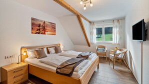 A bedroom with a bed, bedside table, lamp, and a painting of a sunset.