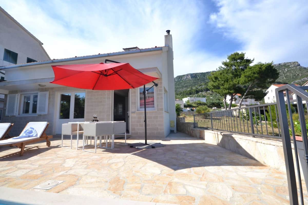A stone patio with a red umbrella, a table, and lounge chairs.