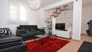 A modern living room with a black leather sofa, a glass coffee table, and a red rug. There is a white staircase with a TV on the upper landing. - Marvelous Escape Bol Island Villa With Pool (Bol)