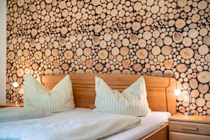 A bedroom with a wooden headboard, two pillows, a bedside lamp, and a wall covered with wooden logs.
