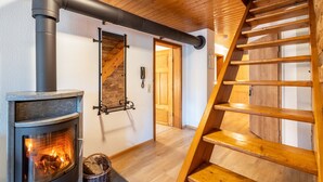 Une pièce dotée d’un poêle à bois, d’un escalier en bois et d’une porte donnant sur une autre pièce.