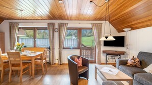 Une pièce chaleureuse avec un plafond en bois, un coin repas avec une table et des chaises, un canapé et un téléviseur.