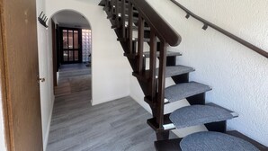 A staircase with a wooden handrail and grey carpeted steps leading to an upper floor.