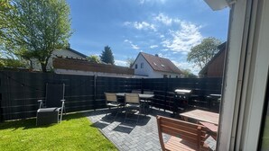 A patio with a table and chairs, a grill, and a view of a house in the background.