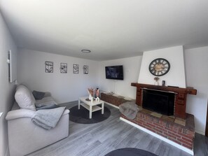 Ein Wohnzimmer mit einer Couch, einem an der Wand befestigten Fernseher, einem Kamin und einer Uhr.