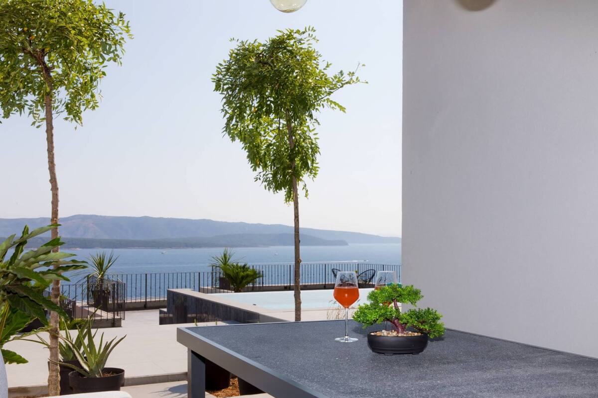 A balcony with a view of the sea, a table with a potted plant, and a chair.