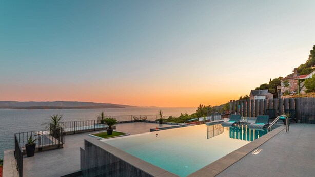 Piscina infinita no terraço com vista para o mar ao pôr do sol.