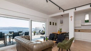 Sala de estar moderna com sofá de couro, área de jantar e vista para o mar.
