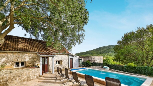 A stone building with a swimming pool, outdoor seating, and a view of hills.