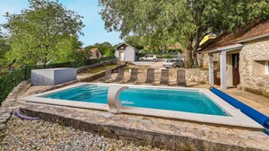 A rectangular swimming pool with a stone border, surrounded by pebbles. There are lounge chairs along the poolside.