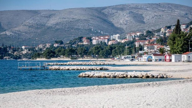 A coastal town with a rocky beach, a pier, and buildings in the background. - Charming and Cozy Okrug Gornji Apartment With Balcony (Okrug)
