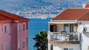A coastal town with buildings overlooking the sea, featuring balconies with outdoor furniture and a satellite dish. - Charming and Cozy Okrug Gornji Apartment With Balcony (Okrug)