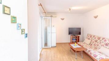 Una sala de estar con un sofá, un televisor y una mesita de centro. Hay cuadros enmarcados en la pared y una puerta corrediza que da a otra habitación.